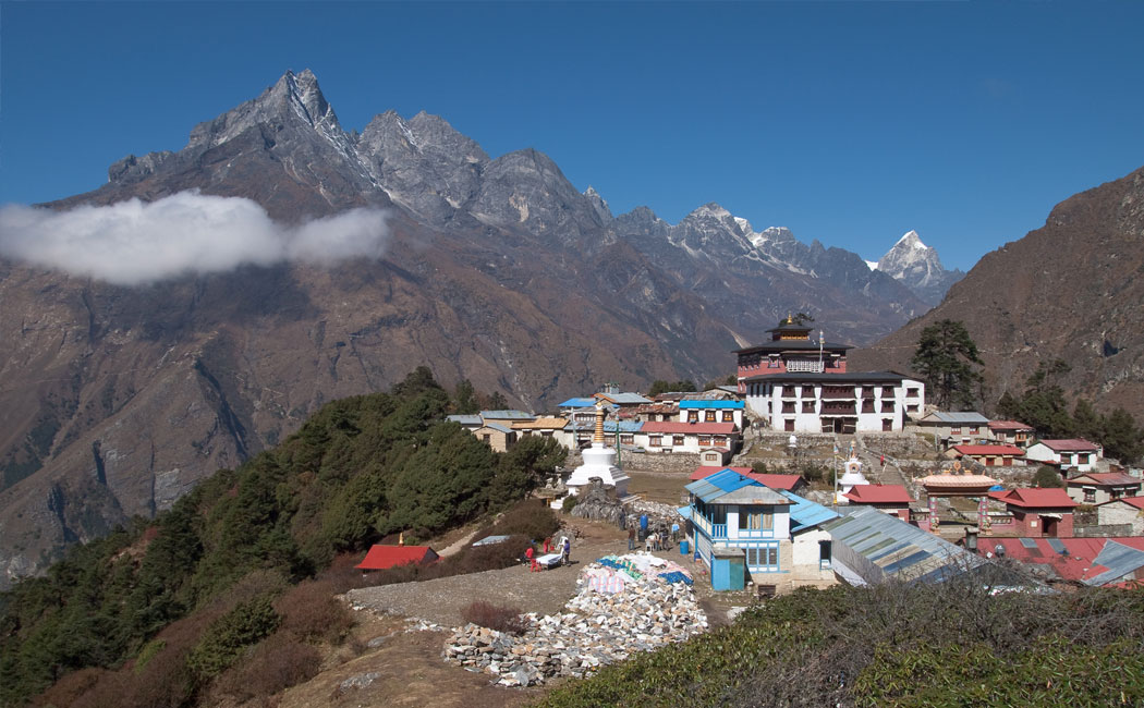 Tengboche Monastery in Nepal's Everest region with Buddhist stupas, colorful buildings, and towering Himalayan mountains under a clear blue sky.