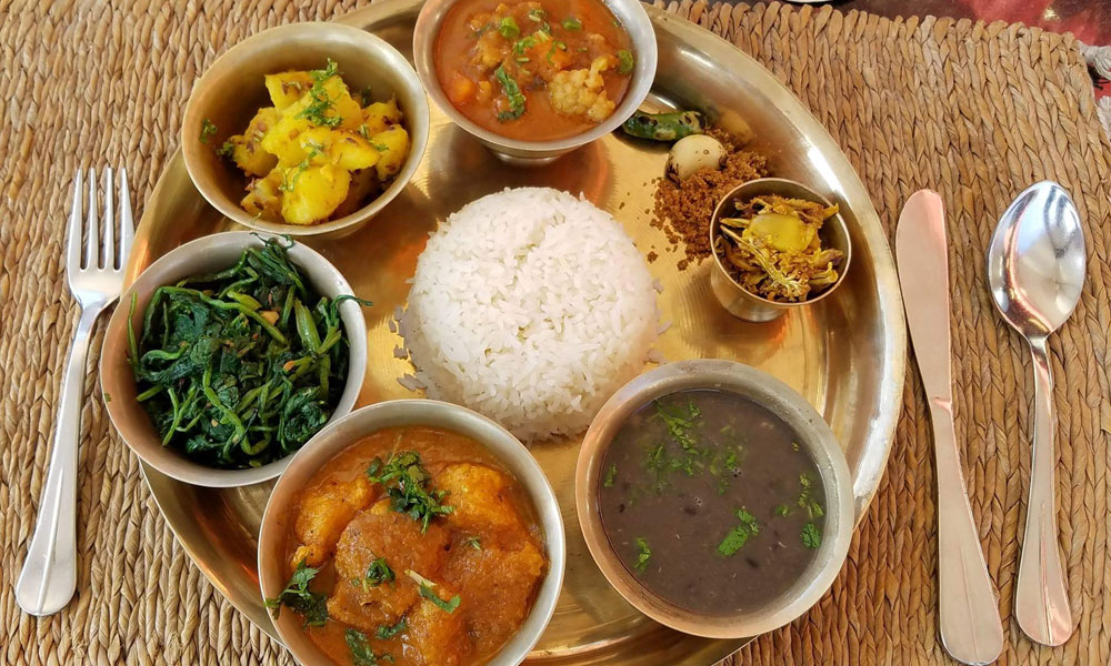 Traditional Nepali dal bhat with rice, lentil soup, vegetable curry, greens, and side dishes on a metal platter.
